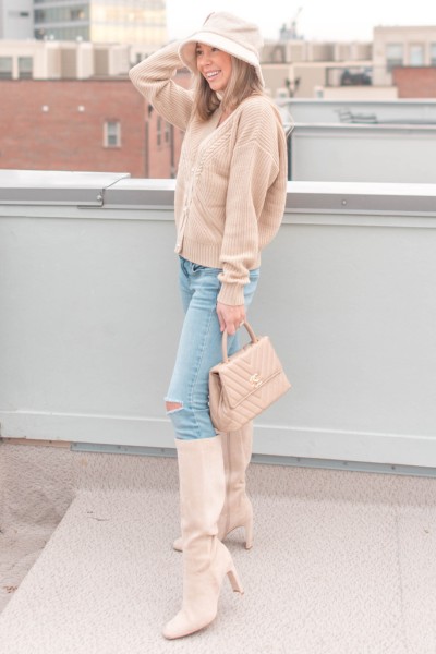 A woman wears beige cowboy boots, sweater and ripped jeans