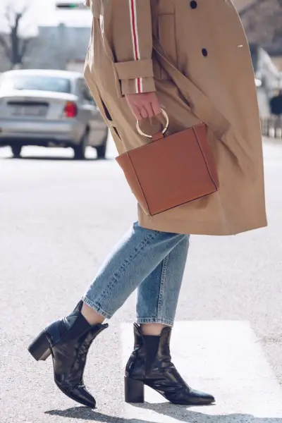 A woman wears black boots with jeans and long blazer