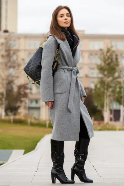 A woman wears black cowboy boots and grey trench coat