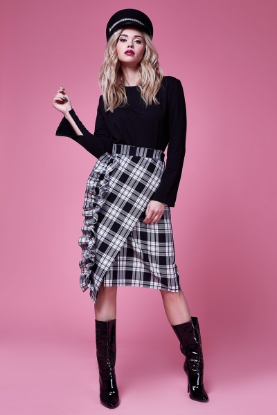 A woman wears black cowboy boots, plaid skirt and long sleeves top