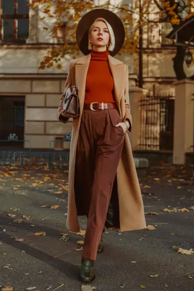 A woman wears black cowboy boots, trouser, blazer and a sweater.