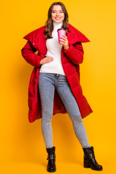A woman wears black cowboy boots with jeans, white turtleneck, red coat