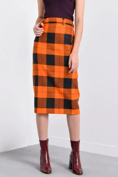 A woman wears brown ankle boots with plaid skirt and black top