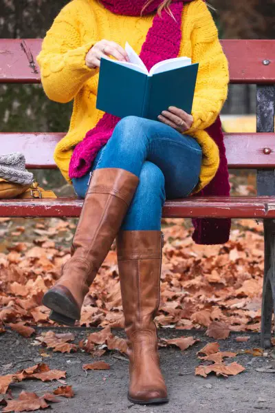 A woman wears brown cowboy boots, jeans, yellow sweater and red scarf