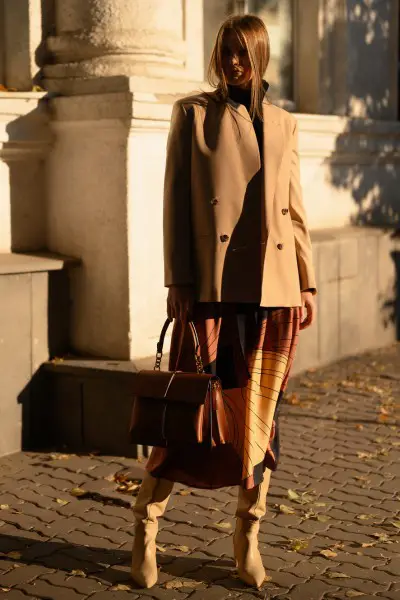 A woman wears cowboy boots, dress and suit coat