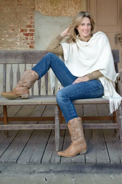 A woman wears cowboy boots with denim jeans, sweater and cardigan