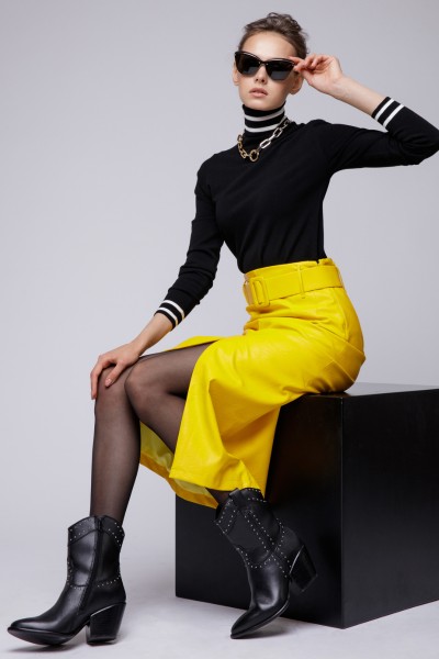 A woman wears cowboy boots with tights, yellow skirt and turtleneck