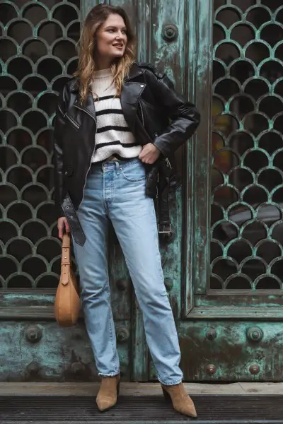 A woman wears jeans, leather jacket and is holding a bag