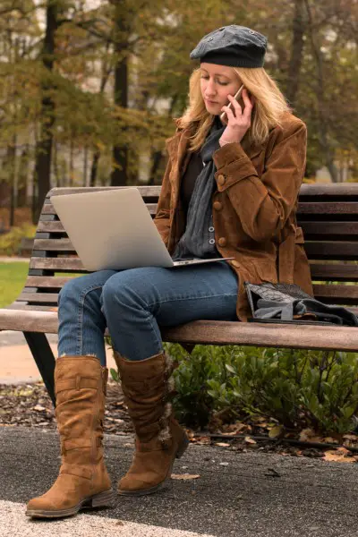 A woman wears leather calf, leather coat, denim jeans, scarf and is working on the park