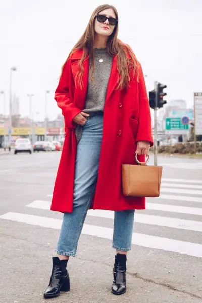 A woman wears red trench coat, blue jeans, sweater and black ankle boots