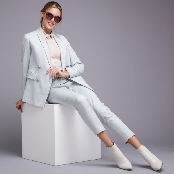 A woman wears short white cowboy boots with a white suit and sunglasses. 