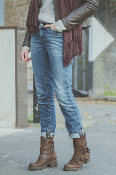 A woman wears sweater, denim jeans, ankle boots with scarf and sweater.