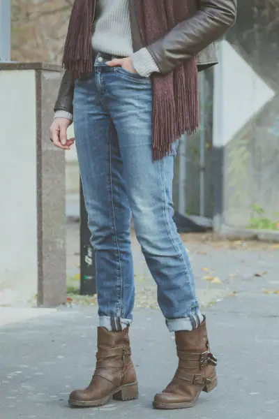 A woman wears sweater, denim jeans, ankle boots with scarf and sweater.