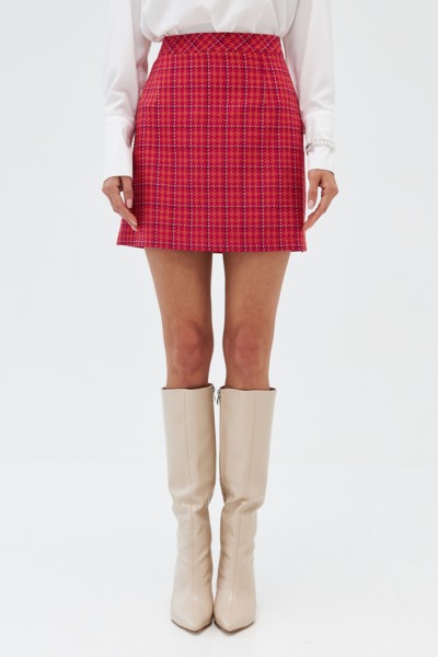 A woman wears white cowboy boots, plaid red skirt and cowboy boots