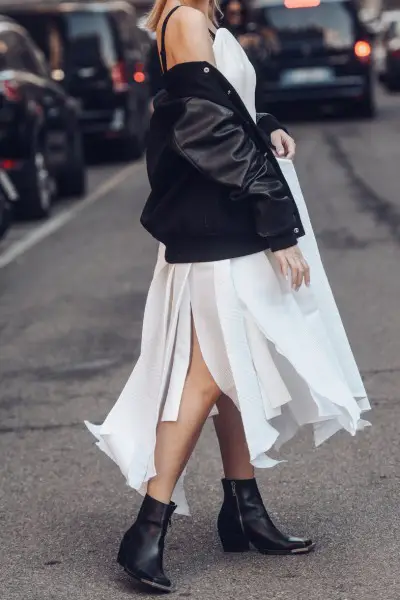 A woman wears white dress, black coat with cowboy boots