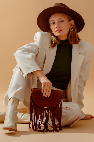 A woman wears white suits with white cowboy boots, wide brim hat and finge handbag