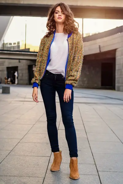 A woman wears white tee, bomber jacket, blue jeans and cowboy boots
