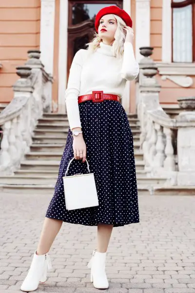 A woman weasr white short cowboy boots, skirt, sweater and beret