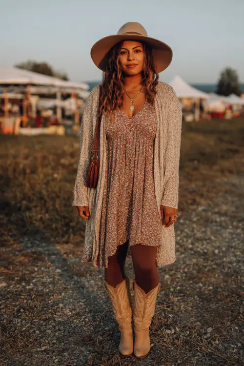A curvy woman wears a soft floral chiffon dress over ribbed leggings with classic tan cowboy boots, styled with a long cozy cardigan, wide-brim felt hat and crossbody bag