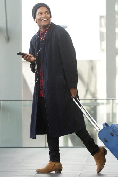 A man wears black jeans with brown cowboy boots and coat