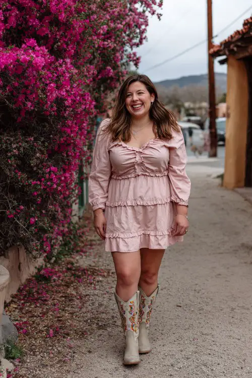 A plus-size woman wears a light pink ruffled dress with embroidered tall cowboy boots