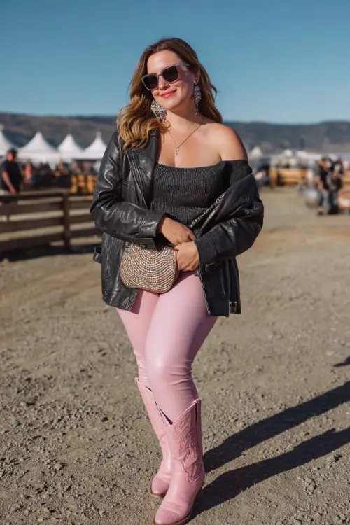 A plus-size woman wears bubblegum pink cowboy boots with faux-leather leggings, a fitted off-shoulder knit top and cropped leather jacket, finished with a mini shoulder bag and bold earrings
