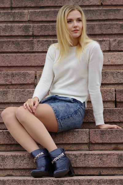 A woman wears a denim skirt with black ankle cowboy boots and white long sleeves tee