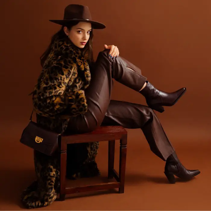 A woman wears a leopard fur coat with brown cowboy boots and brown leather pants