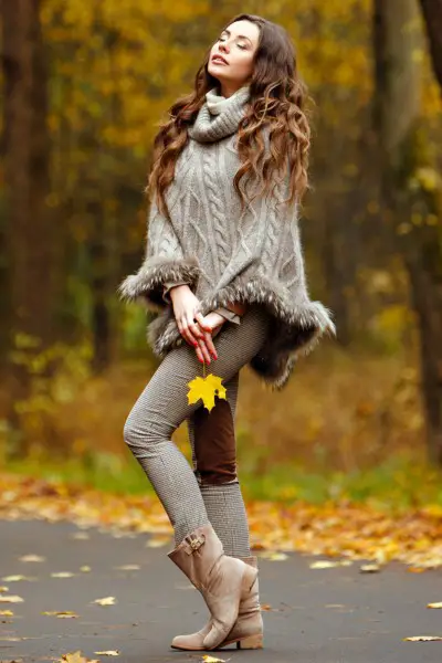A woman wears beige cowboy boots with skinny pants and oversize sweater