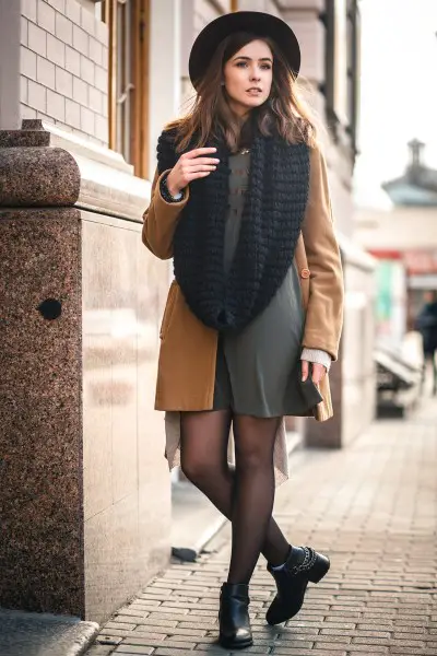 A woman wears black ankle cowboy boots with dress, coat and large scarf