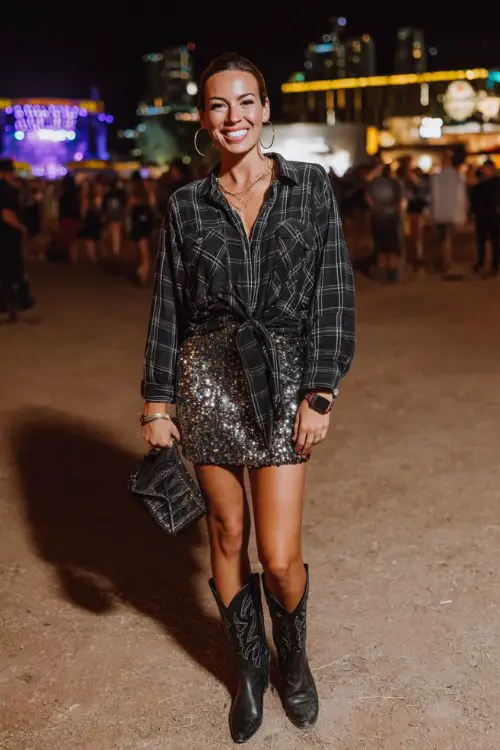 A woman wears black cowgirl boots with a sequin mini skirt and oversized flannel shirt tied at the waist, accessorized with hoop earrings and a sleek clutch