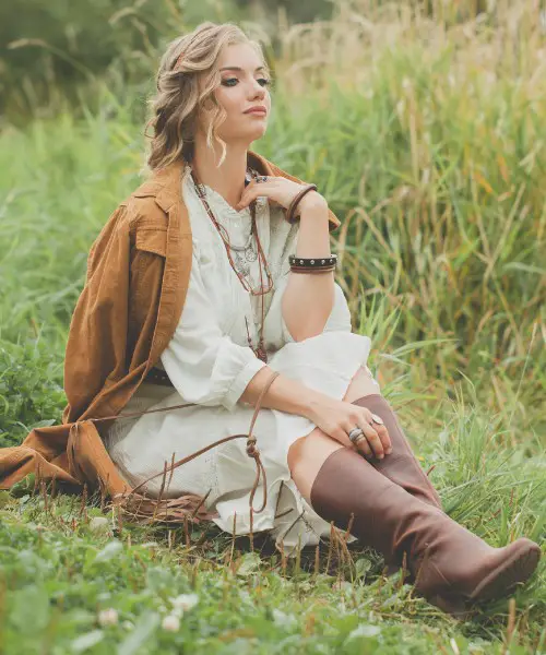 A woman wears brown boots, coat and white dress