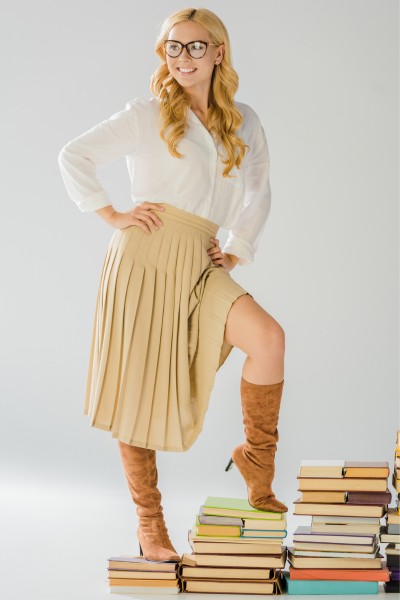 A woman wears brown boots, pleated skirt and blouse