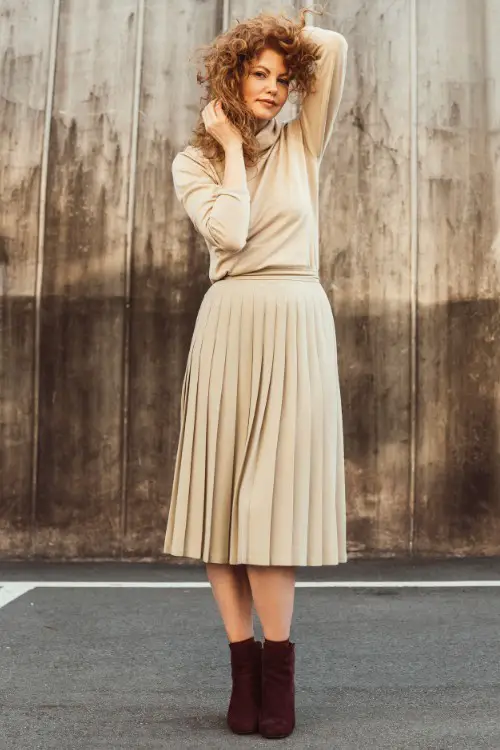 A woman wears brown cowboy boots with a pleated skirt