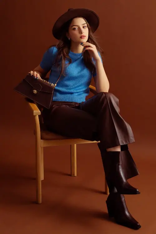 A woman wears brown cowboy boots with blue sweater top and leather pants