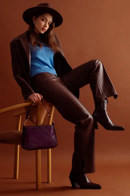 A woman wears brown cowboy boots with leather pants, a leather coat and blue top