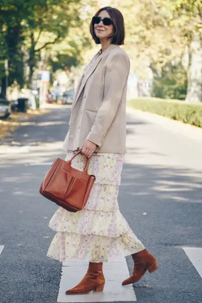 A woman wears cowboy boots with a layered dress and blazer