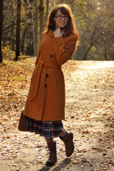 A woman wears cowboy boots with a long coat and a plaid dress