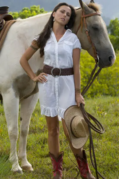 A woman wears cowboy boots with white dress and leather belt