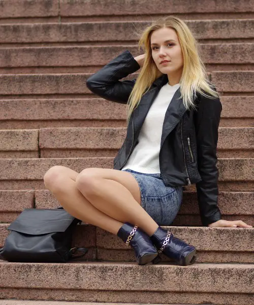 A woman wears denim mini skirt, a black coat and a white t-shirt