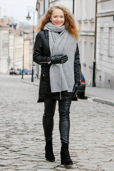 A woman wears legging, boots with black coat and large scarf