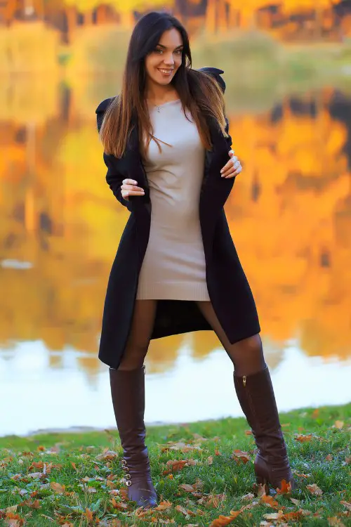 A woman wears tall cowboy boots with a dress and a long coat