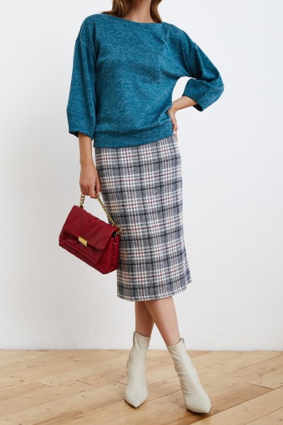 A woman wears white cowboy boots with plaid skirt, top and handbag