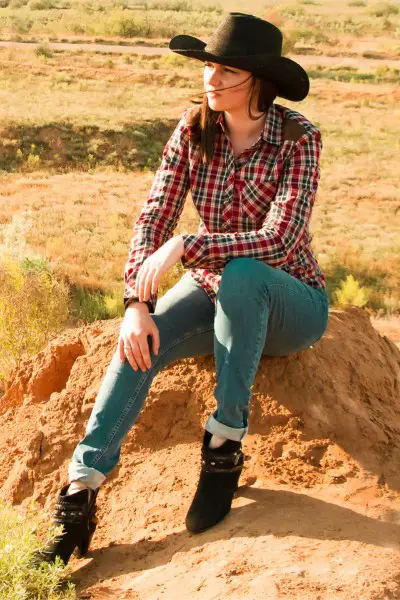 a woman wears jeans, cowboy hat, cowboy boots and plaid shirt