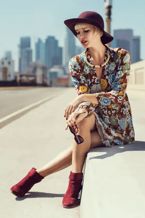 A woman wears a floral dress with a red hat and a red suede boots