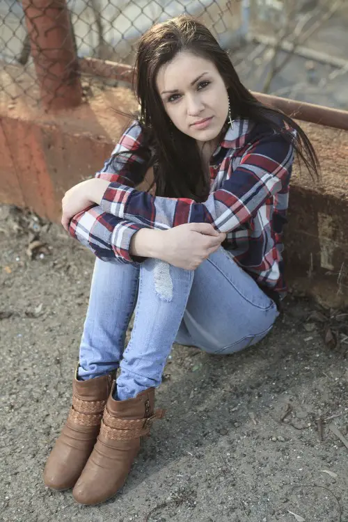 A woman wears a plaid shirt wth jeans and brown cowboy boots