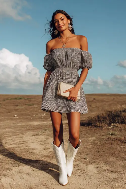 A woman wears a smocked off-shoulder dress with white cowboy boots, styled with hoop earrings and a soft clutch