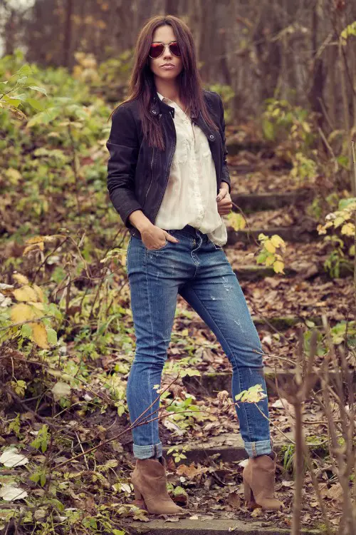 A woman wears ankle cowboy boots with jeans, white top and a coat