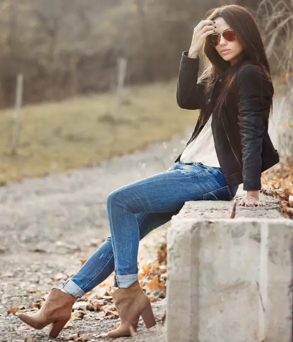 A woman wears ankle cowboy boots with white top, jeans and leather jacket