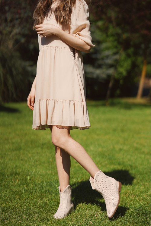 A woman wears beige dress with ankle cowboy boots